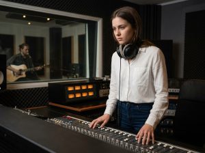 Jeune femme en formation audio découvrant une console de mixage professionnelle dans un studio d'enregistrement